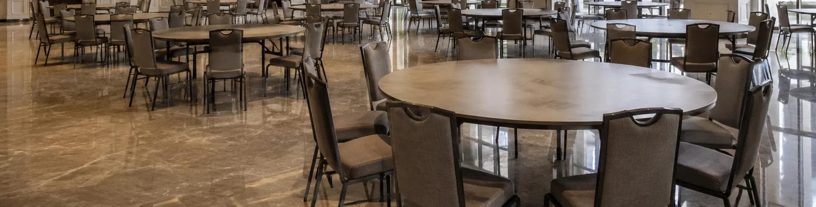 A room of plain round tables and chairs arranged for an event, marble floor reflecting daylight.